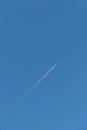 Color outdoor image of a white single isolated airplane with intense contrails in front of a sunny clear deep blue sky Royalty Free Stock Photo