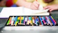 Color pencil Crayons of various colors in a palette box, on the table, against the backdrop of a blurry girl drawing with colors Royalty Free Stock Photo