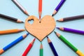 Color pencils in arrange in color wheel colors around wooden heart on blue background. Royalty Free Stock Photo