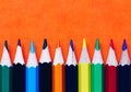 Color pencils isolated on orange background. Close up of colored rainbow pencils for drawing, concept of preparing for school and Royalty Free Stock Photo