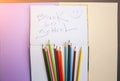 Color pencils lying on pastel purple and beige background. Squared notebook with back to school concept sign and smile. Colorful