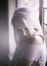 Beautiful blonde woman seated next to window in soft natural light Royalty Free Stock Photo