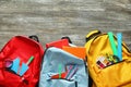 Color rucksacks with school stationery on wooden background