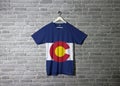 Colorado flag on shirt and hanging on the wall with brick pattern wallpaper. The states of America Royalty Free Stock Photo