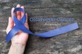 Colorectal or Colon cancer awareness dark blue ribbon on helping hand on old aged wood