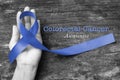Colorectal or Colon cancer awareness with dark blue ribbon on helping hand on old aged wood