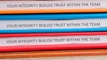 Colored binders stacked on a surface display the message emphasizing the importance of integrity for fostering trust