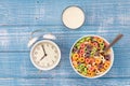 Colored breakfast cereals, alarm clock and glass of milk on a wooden background. Royalty Free Stock Photo