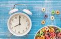 Colored breakfast cereals in a bowl and alarm clock on a blue wooden background. Royalty Free Stock Photo
