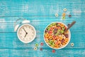 Colored breakfast cereals in a bowl and alarm clock on a blue wooden background. Royalty Free Stock Photo