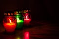 Colored burning votive candles in the dark