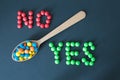 Colored candies dragees lie in a wooden spoon, on the sides of the word yes and no, on a black background