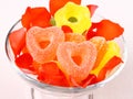 Colored candies with two red hearts in glass bowl and rose petals Royalty Free Stock Photo