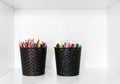 Colored pencils and pens in black containers on a white shelf Royalty Free Stock Photo