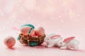 Colored decorated eggs in small basket and porcelain bunnies on pink background.
