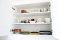 Colored dishes on shelves in an open white kitchen cabinet. Royalty Free Stock Photo
