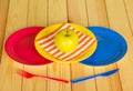Colored disposable plates, plastic knife, fork, apple on light wood. Royalty Free Stock Photo