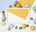 Colored Easter eggs around a wooden white frame on a white, yellow and blue background. Happy Easter. Royalty Free Stock Photo