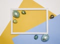 Colored Easter eggs around a wooden white frame on a white, yellow and blue background. Happy Easter. Royalty Free Stock Photo