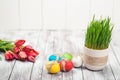 Colored easter eggs, flower pot with green grass and beautiful tulips on wooden background. Royalty Free Stock Photo