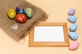 Easter eggs on a sackcloth bag and a frame on the beige background.
