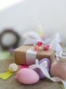 Colored eggs, gift box, rose jam jar on burlap fabric in front of white wall.