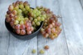 Colored grapes in a black bowl on a gray wooden table,nearby branch of red grape Royalty Free Stock Photo