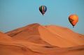 Colored hot air balloons flying over the sand dunes at sunset