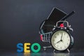Colored letters of SEO with clock, magnifying glass, smartphone, gears in a basket on a black background Copy space Royalty Free Stock Photo