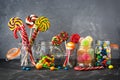 Colored lollipops, colorful round candies and marmalade in glass jars on a black stone table with a gray backdrop. Selective focus