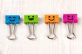 Colored metal binder clips of blue, green, pink and orange color smiles on white wooden background with copy space Royalty Free Stock Photo