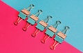 Colored paper clips on two backgrounds in half-pink and blue. Stationery Royalty Free Stock Photo