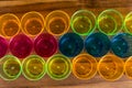 Colored party cups - yellow, orange, pink and blue lined in three rows on a wooden board