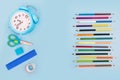 Colored pencils alarm clock and miscellaneous school supplies on a blue background. School concept