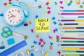 Colored pencils alarm clock and miscellaneous school supplies on a blue background. School concept