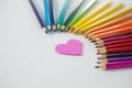 Colored pencils arranged in semi circle with heart on white background Royalty Free Stock Photo