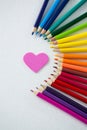 Colored pencils arranged in semi circle with heart on white background Royalty Free Stock Photo