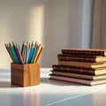 Colored pencils arranged in a wooden cup and a stack of notebooks with leather-like covers sit on a white desk. Royalty Free Stock Photo