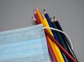 Handful of colored pencils inside the elastic rubber of a surgical mask. Royalty Free Stock Photo