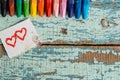 Bright colored pencils on an old blue green wooden background. Two red hearts painted on a slice of paper Royalty Free Stock Photo