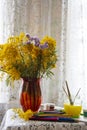 Colored pencils, markers, and paint next to a bouquet of Mimosa in a red vase on a lace tablecloth Royalty Free Stock Photo