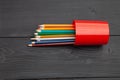 Overturned red glass with colored pencils on a dark wooden background