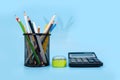 Colored pencils and pens in stand and calculator on a blue background. Royalty Free Stock Photo