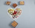 Colored pills in the shape of a heart and different types of nuts on a gray background. Traditional medicine and healthy