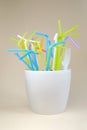 Colored straws for drinks in a pot with earth on a beige background