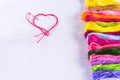 Colored thread for embroidery on white canvas, a needle with red thread in the shape of a heart. The concept of love for a hobby.