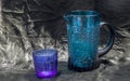 Colored transparent blue glass cup and blue glass jug for water drinking and surface reflections on a black background Royalty Free Stock Photo