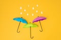 Colored umbrellas on a yellow background and paper raindrops. Conceptuality and place for the text
