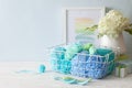Colored yarn in cool shades lies in a white metal basket. Crochet hooks. Hydrangea in a vase in the Nordic style.