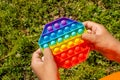 Colorful antistress sensory toy fidget push pop it in kid& x27;s hands. Pop it toy. Girl plays outside.